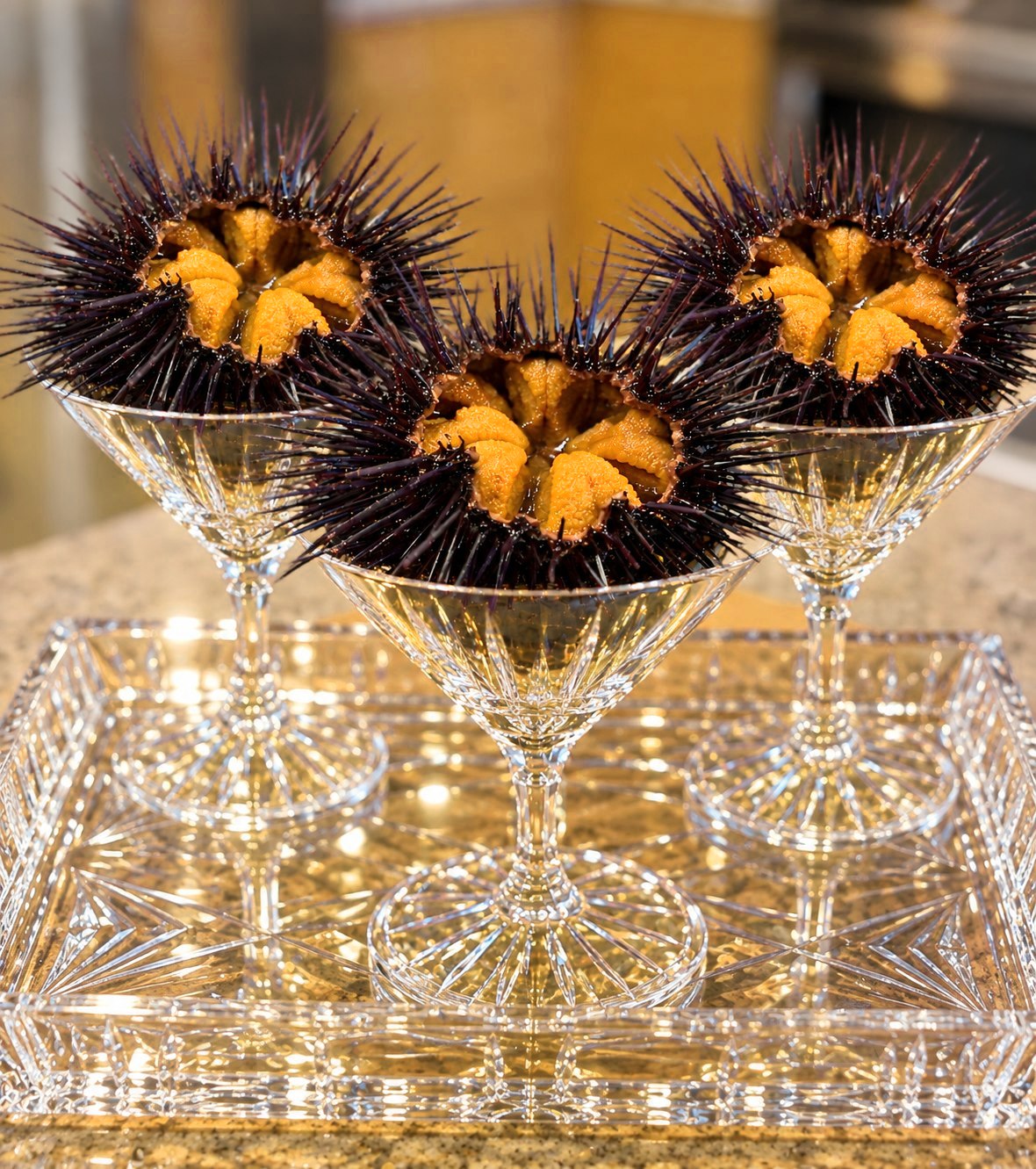 Three opened sea urchins showing fresh uni, served in crystal glasses on a crystal tray
